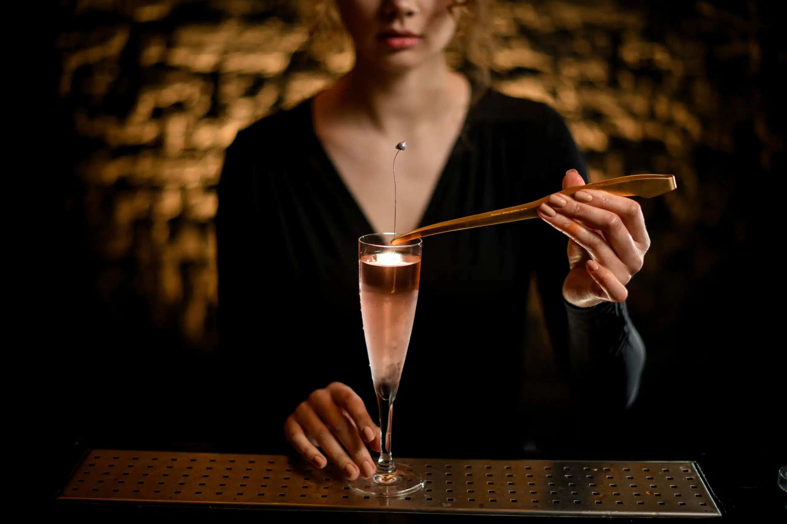 close-up girl at bar hold glass with light rose cocktail and decorates it by flower