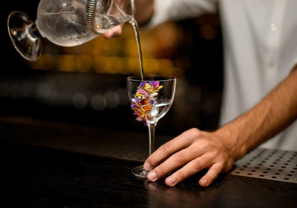 Male bartender in white shirt pours cocktail from glass with strainer